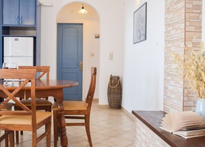 A dining area with a round table and chairs, a blue door, and a kitchen with cabinets. - Dianas Studios (Kefalonia)