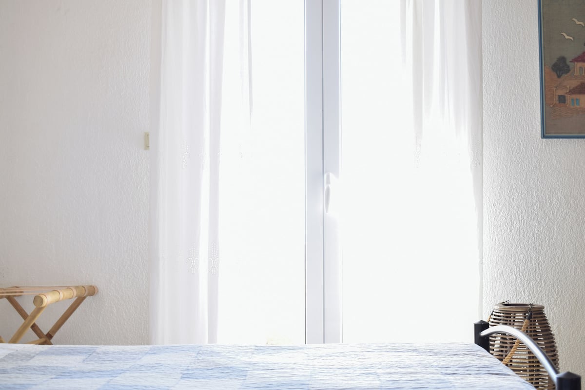 Una habitación con una cama, una silla de madera, una cesta de mimbre y un cuadro en la pared.