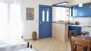 A kitchen with blue cabinets, a tiled backsplash, a stove, and a dining area with a table and chairs. - Dianas Studios (Kefalonia)