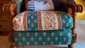 A wooden chair with a patterned cushion and a pillow with text, positioned against a yellow wall. - Symi Garden Studios (Symi)
