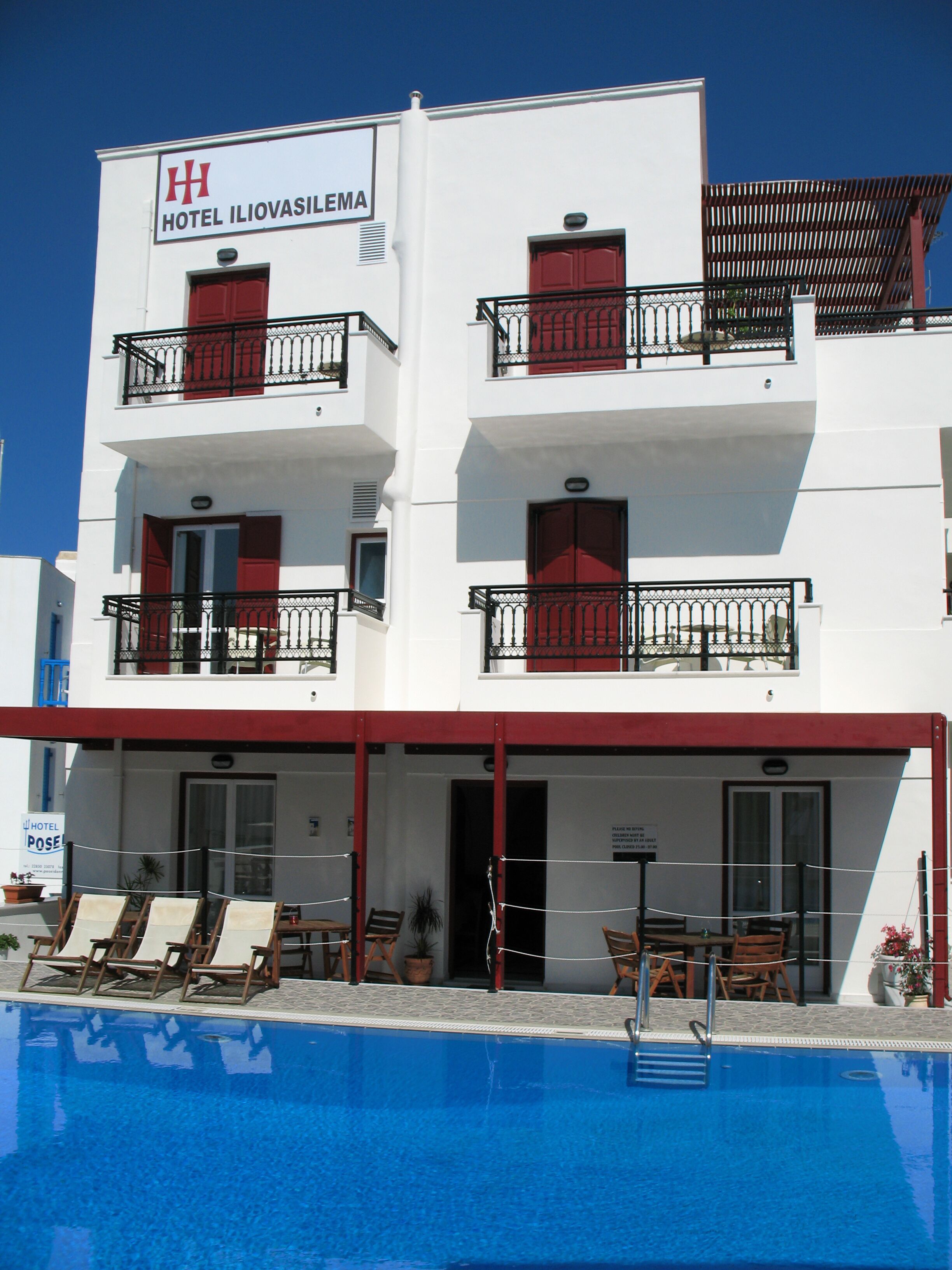 A hotel with a pool area, multiple balconies, and a sign indicating it is Hotel Ilioavasilema.