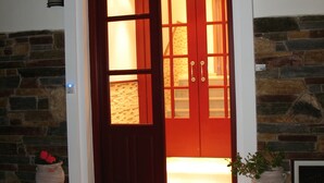 A wooden door with glass panels, a stone wall, and a potted plant beside it. - Iliovasilema (Naxos)