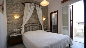 A bedroom with a bed, a nightstand, a wall-mounted light, and a sliding glass door to a balcony. - Iliovasilema (Naxos)