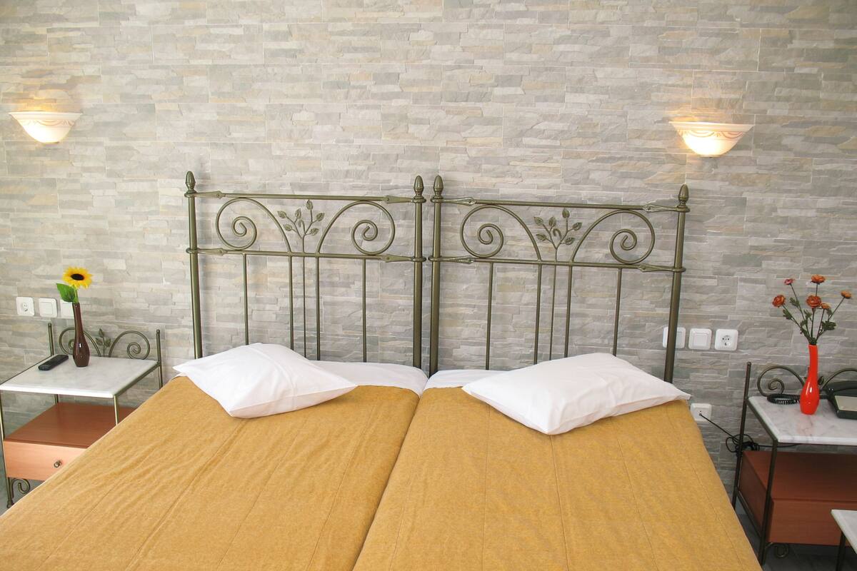 A double bed with a metal headboard, two bedside tables with lamps, and a stone wall.