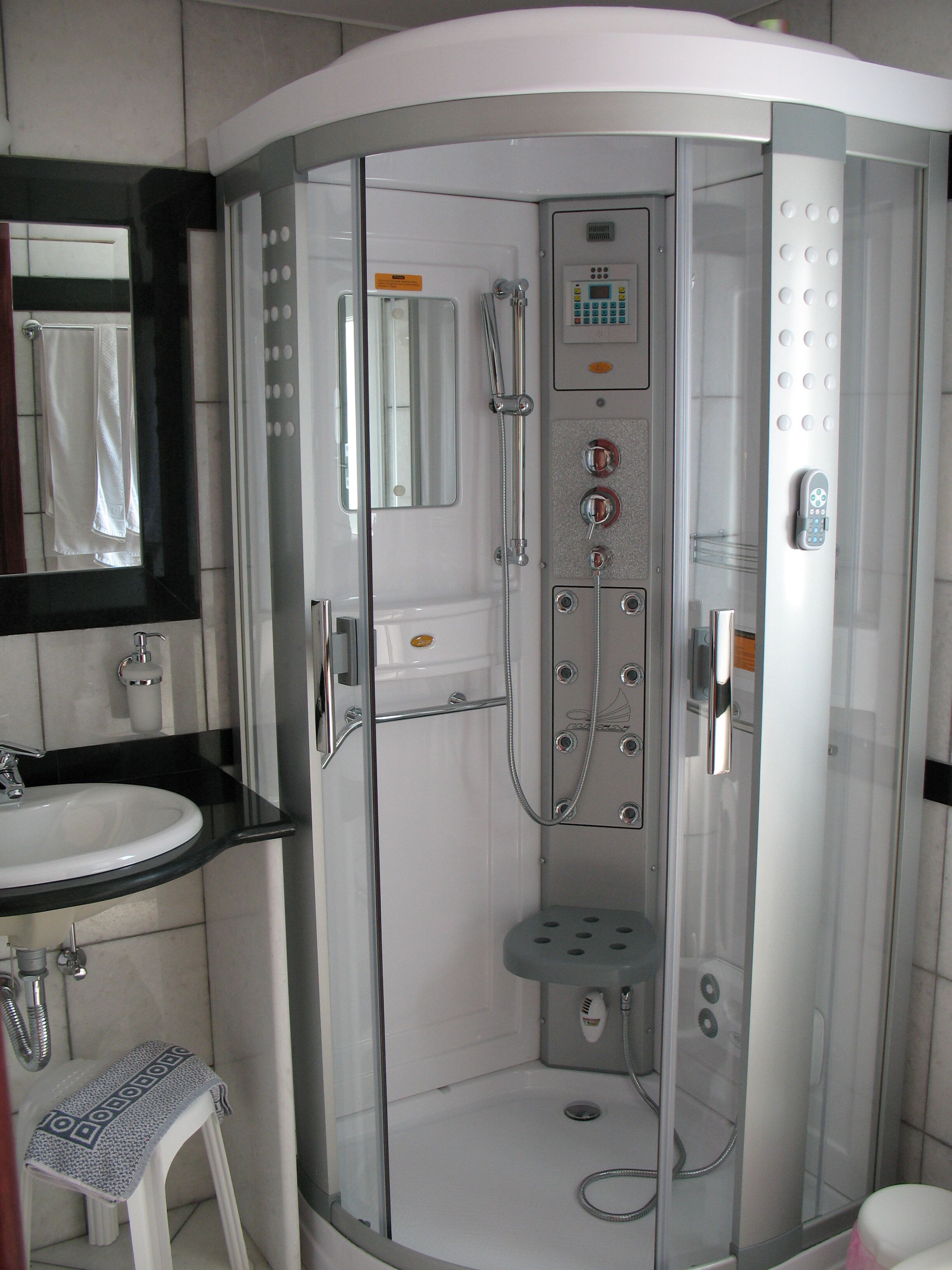Un bany modern amb dutxa d'ús de vidre, un lavabo blanc i un mirall sobre el lavabo.