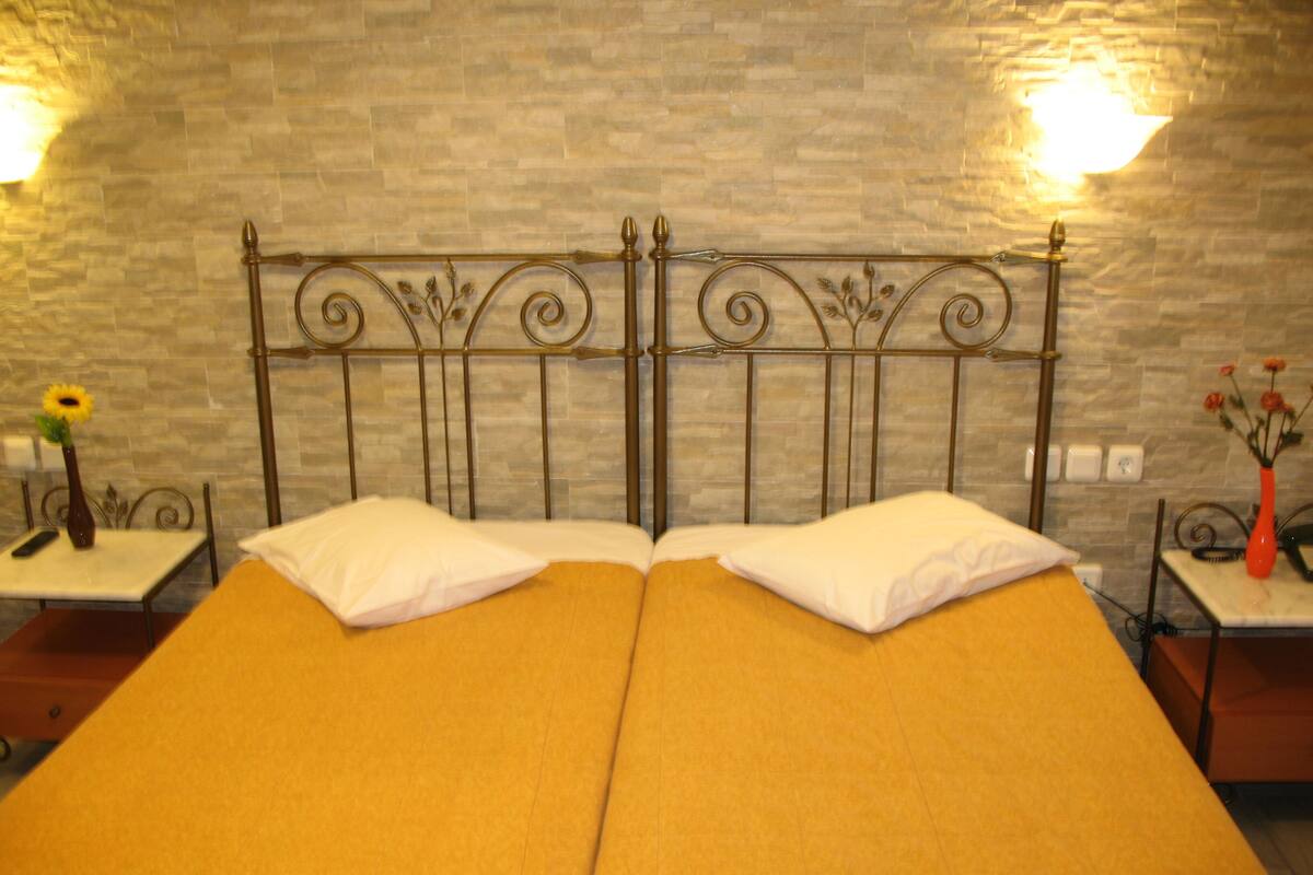A double bed with a metal headboard, two bedside tables with lamps, and a vase with flowers on each side.