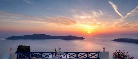 A sunset view from a terrace with a table set for two, overlooking the sea and islands.