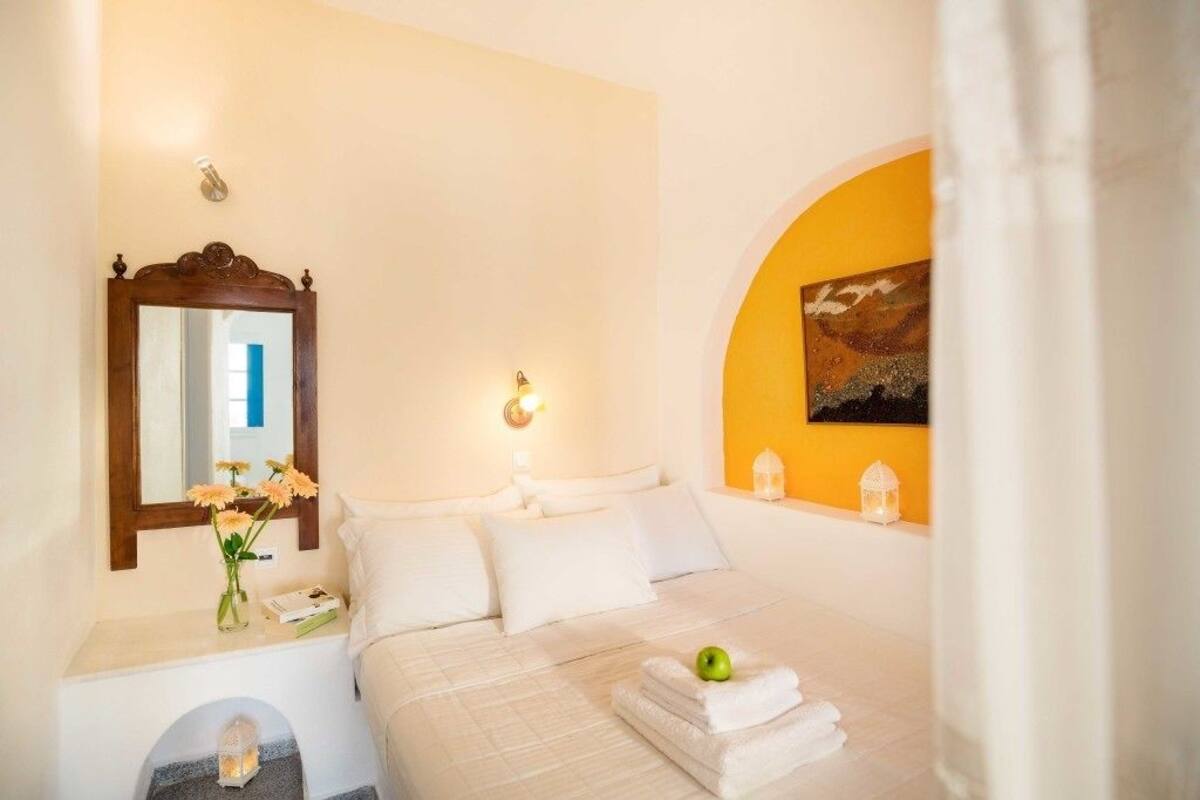 A hotel room with a bed, a nightstand, a mirror, a painting on the wall, and a window with curtains.