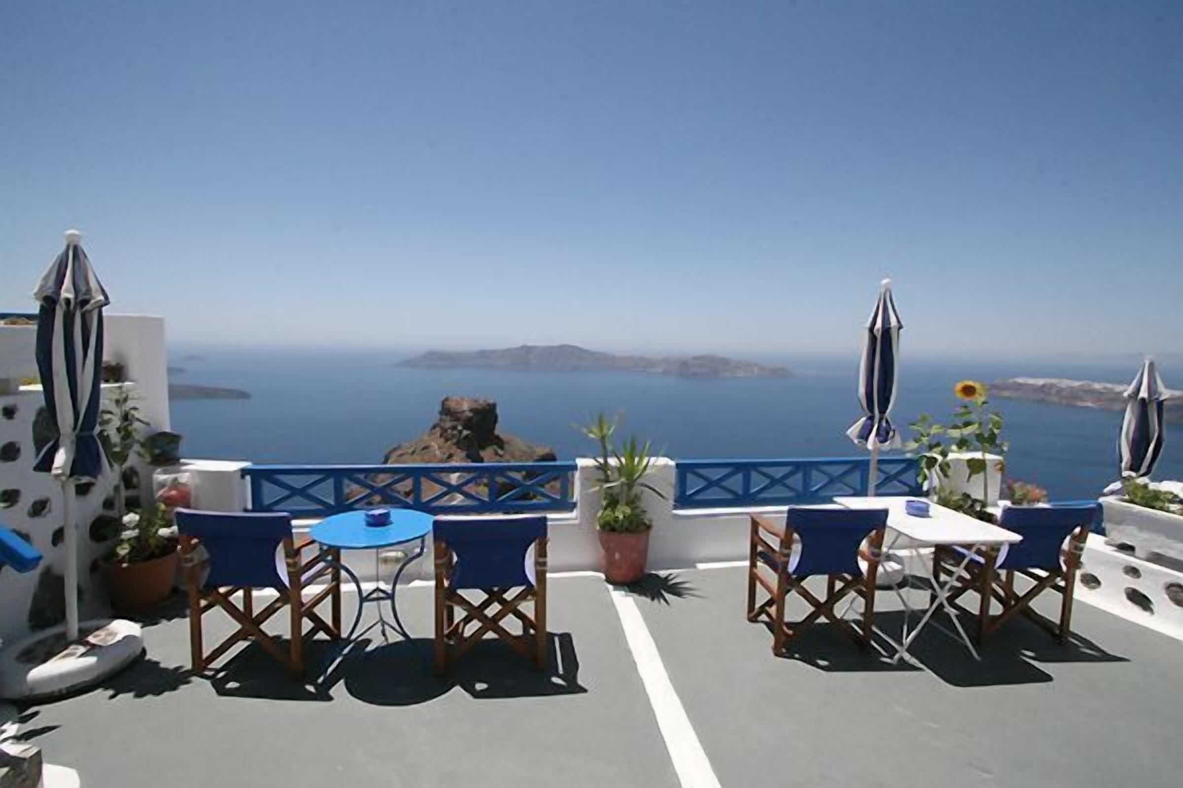 A terrace with blue chairs and tables, potted plants, and a view of the sea.
