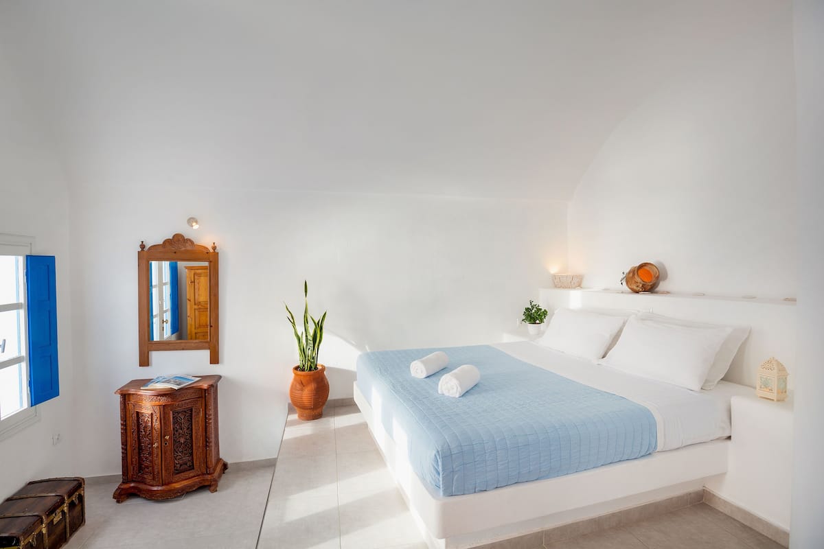 A bedroom with a bed, a wooden cabinet, a mirror, a potted plant, and a small table.