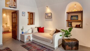 A cozy living room with a sofa, a small table, a plant, and a decorative chest. - Annio Flats (Santorini)