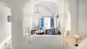 A bedroom with a bed, a nightstand, a lamp, and a window with curtains. - Annio Flats (Santorini)