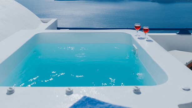 A clear blue sky, a pool with two glasses of red wine, and a view of the sea and islands. - Annio Flats (Santorini)