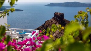 A balcony with white chairs, a small table, and a view of the sea and islands. - Annio Flats (Santorini)