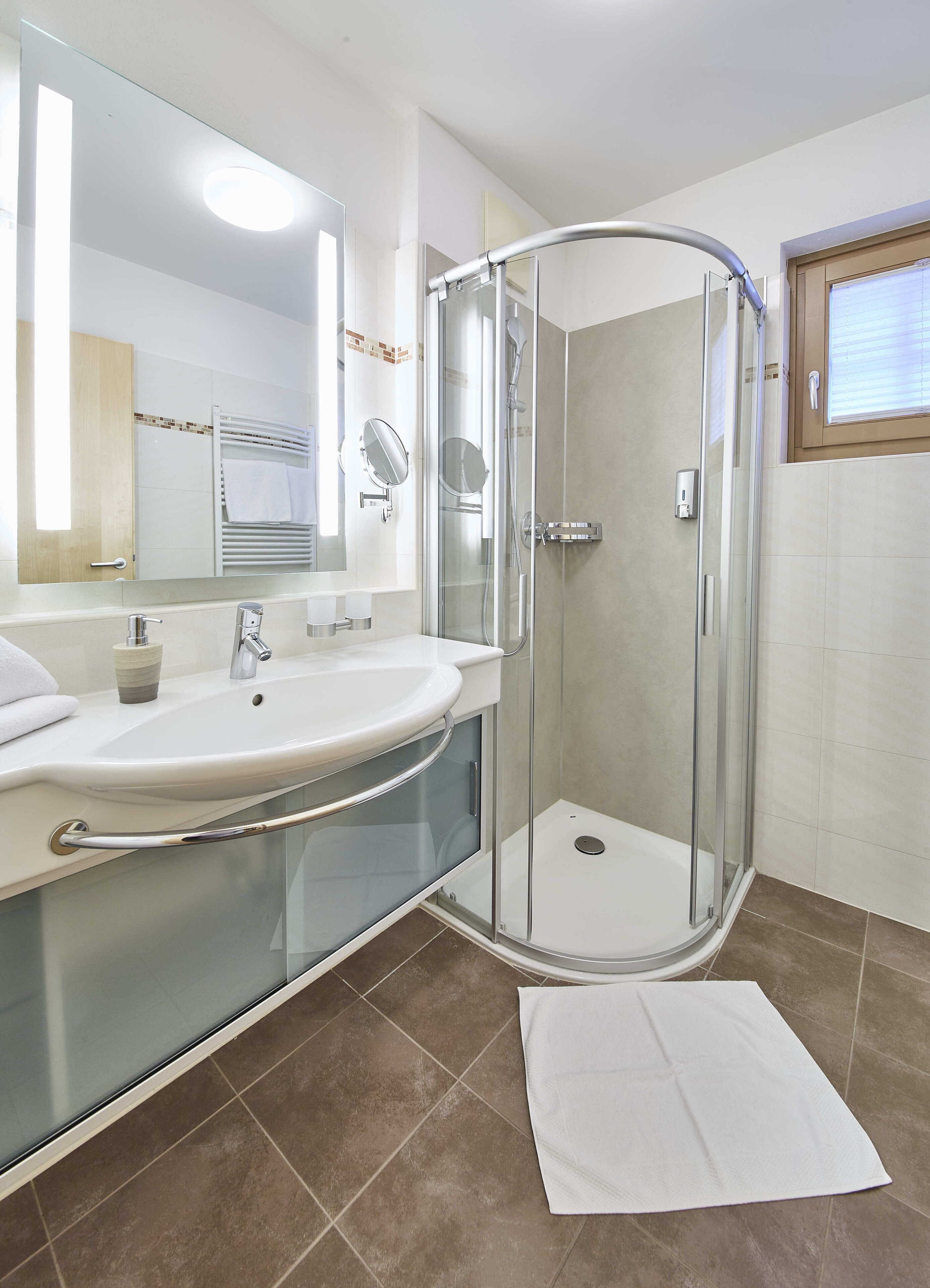 A modern bathroom with a glass-enclosed shower, a white sink with a mirror, and a towel on the floor.