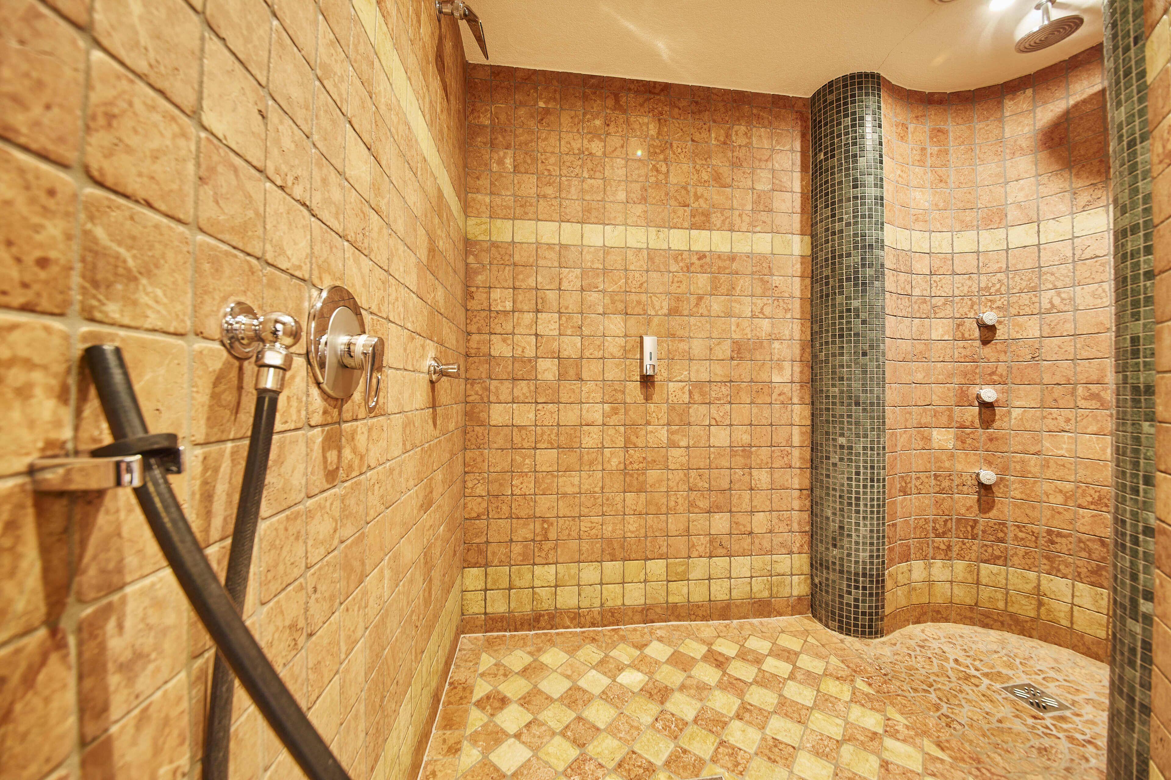 Ducha con piso a cuadros y paredes de azulejos, incluyendo una columna vertical revestida de verde.