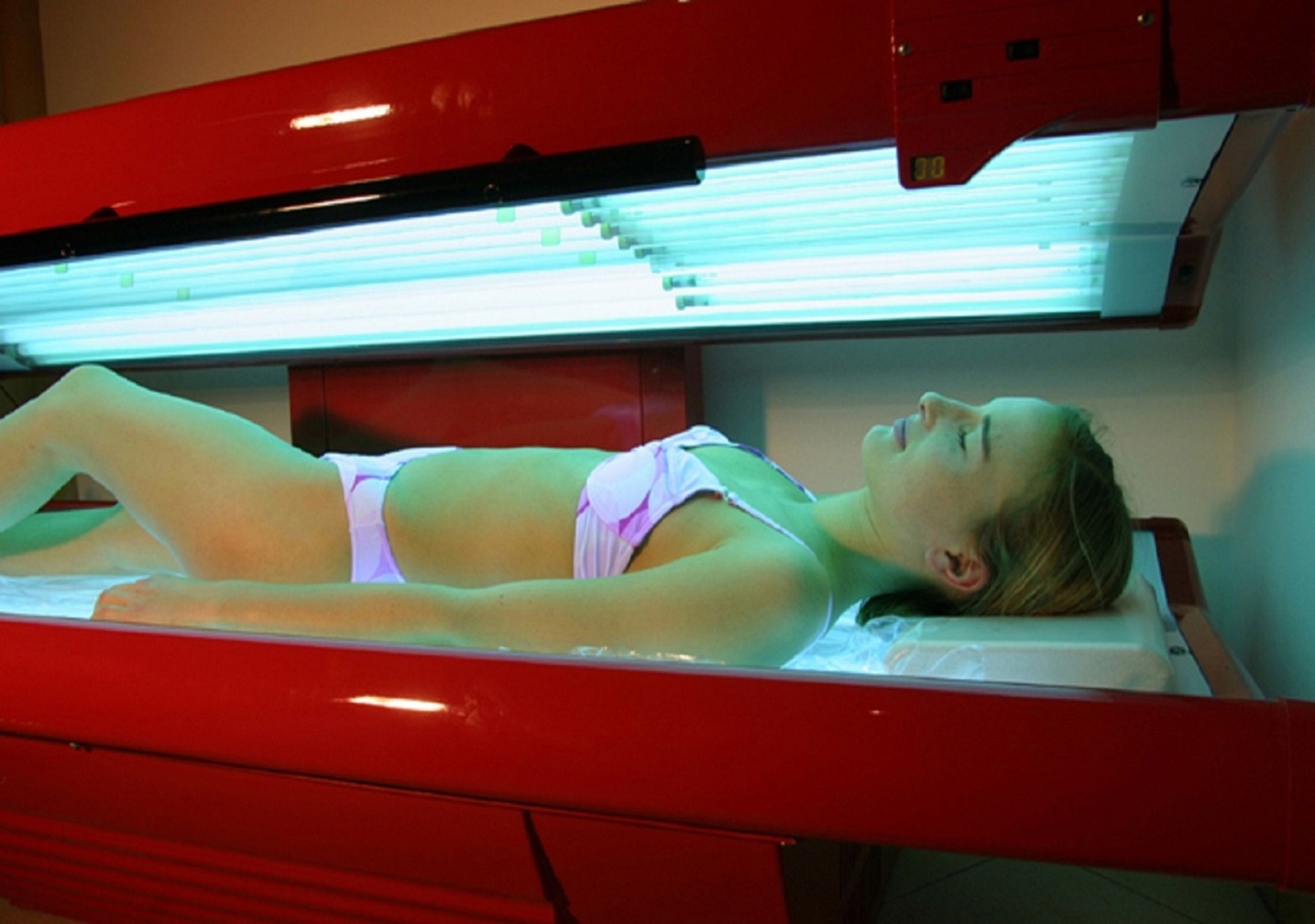 A person lying on a treatment bed under a UV light.