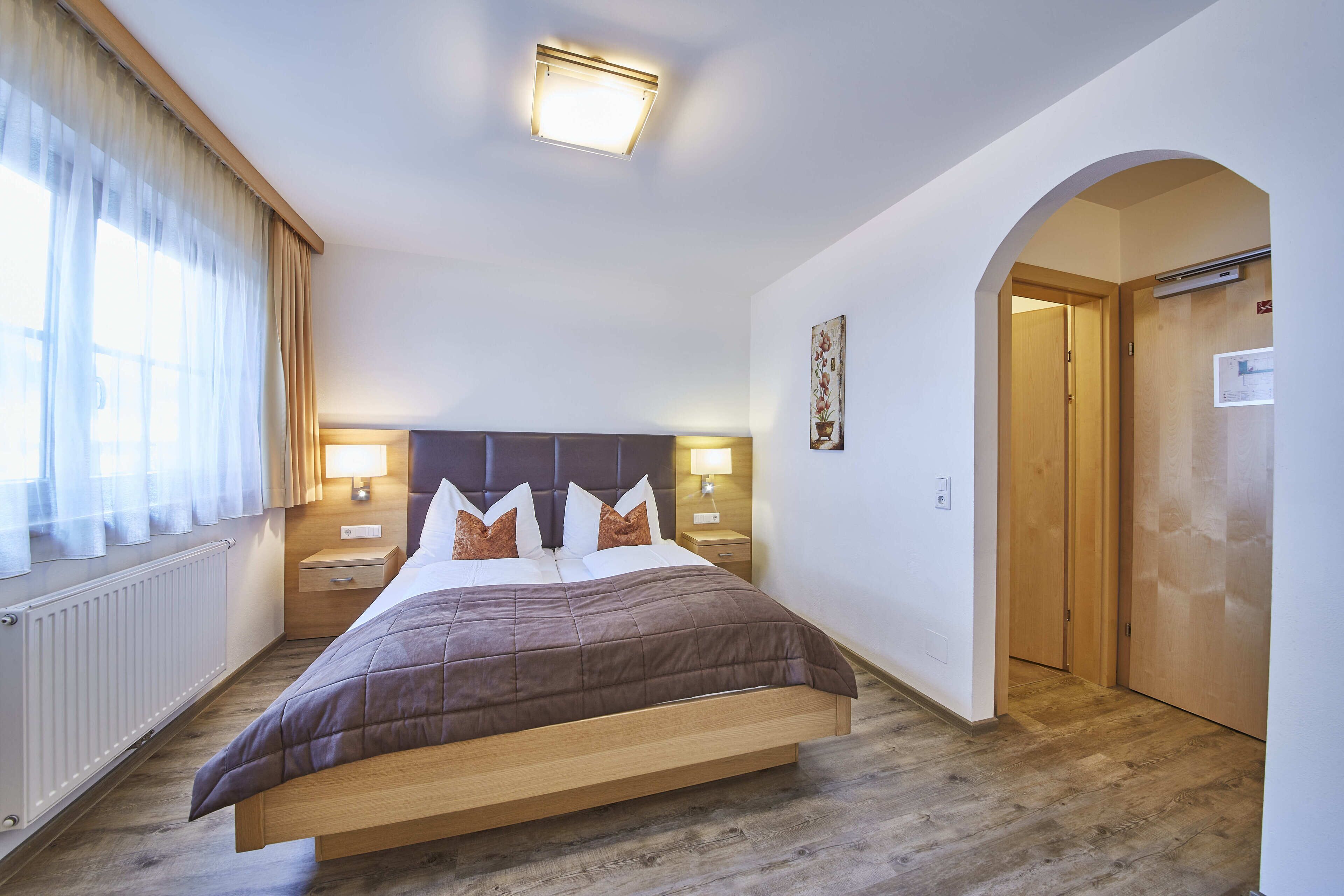 A bedroom with a bed, bedside lamps, a radiator, and a wooden door.