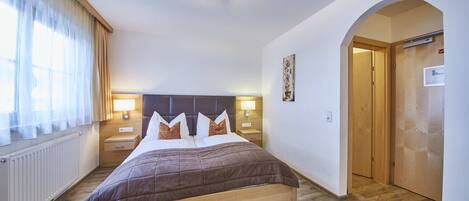 A bedroom with a bed, bedside lamps, a radiator, and a wooden door.