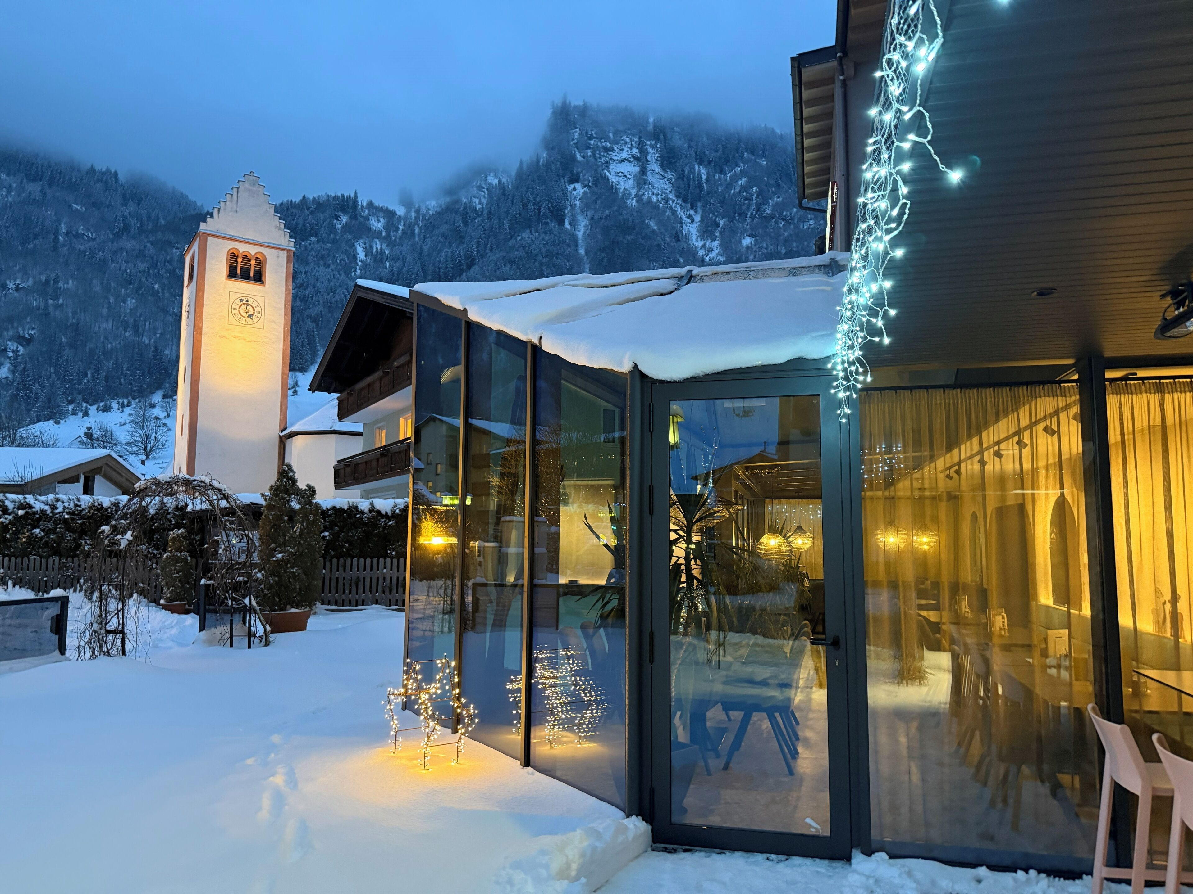 A modern building with large glass windows, a snow-covered landscape, and a clock tower in the background.