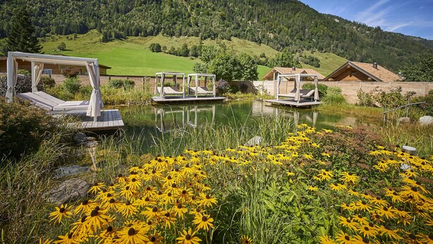 A lakeside view with a wooden cabin and a gazebo by the water. - Hotel Römerhof (Fusch an der Grossglocknerstrasse)