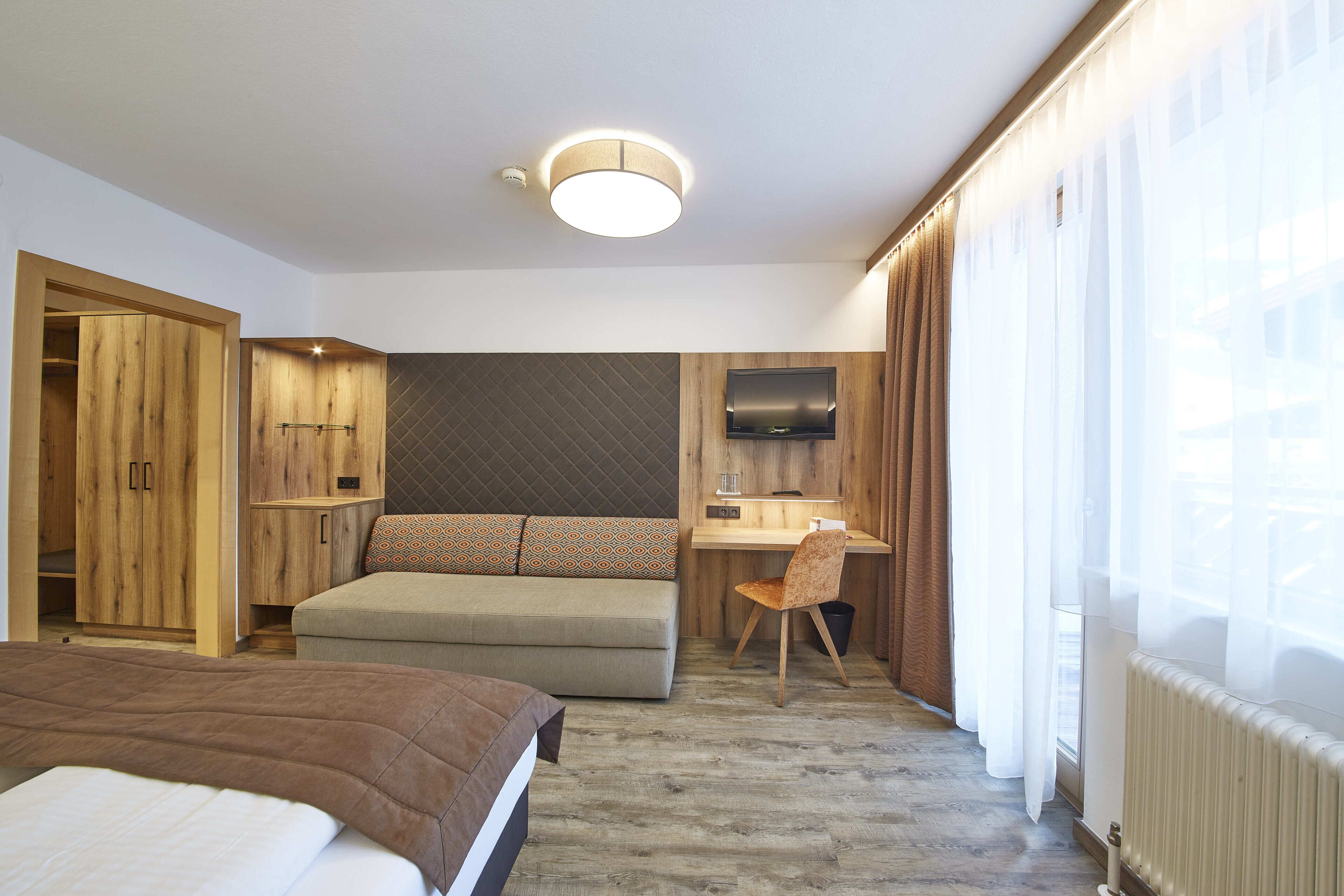 A hotel room with a bed, a desk, a chair, a TV, and a wardrobe.