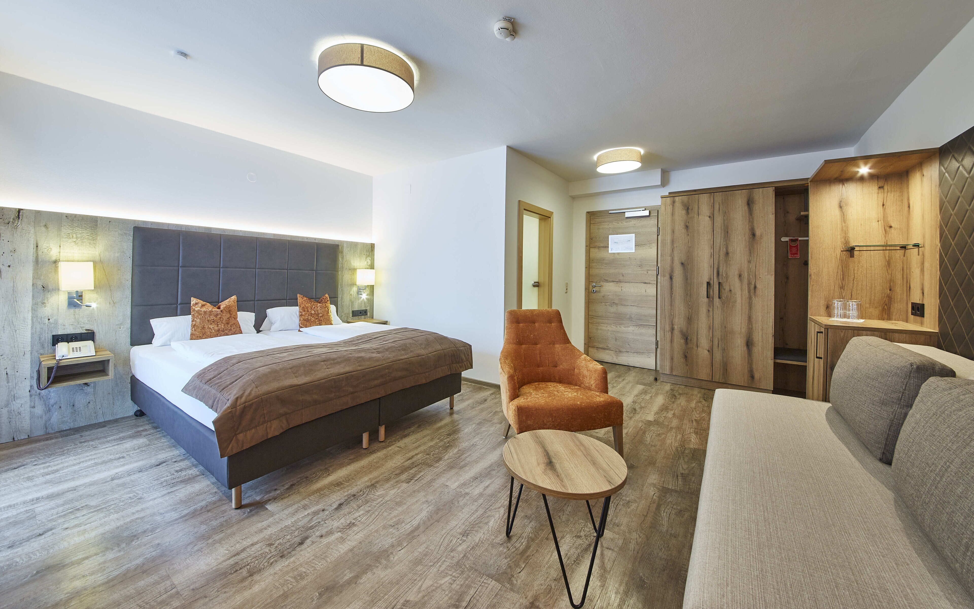 Habitación de hotel moderna con una cama grande, un armario de madera, una mesita redonda pequeña y un sofá.