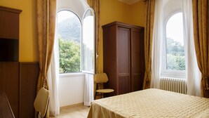Una habitación de hotel con cama, una silla, armario y ventana con cortinas.