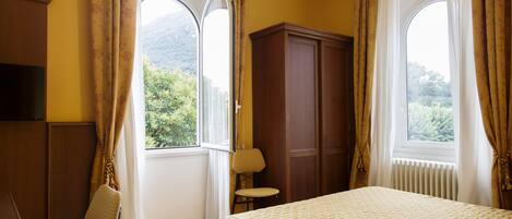 A hotel room with a bed, a chair, a wardrobe, and a window with curtains.