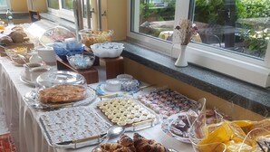 Una mesa de buffet con diversos alimentos, como pasteles y pan, montada cerca de una ventana que ofrece vistas a la vegetación.