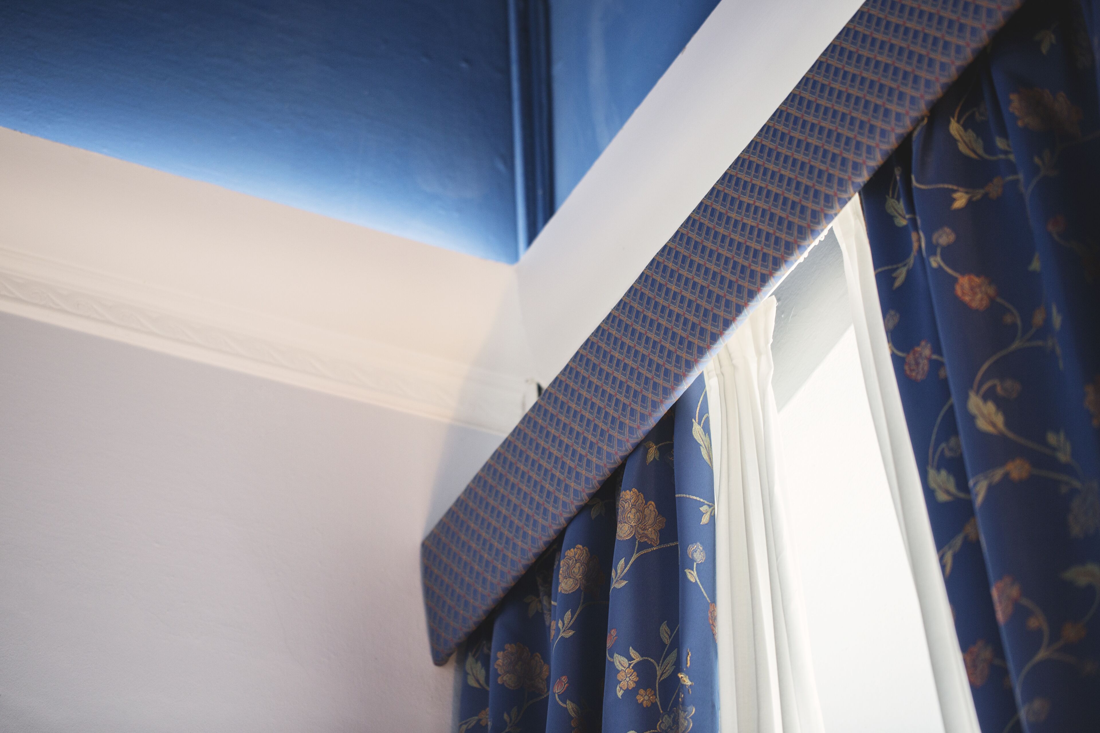 A corner of a room with a white ceiling and a window with blue floral curtains.
