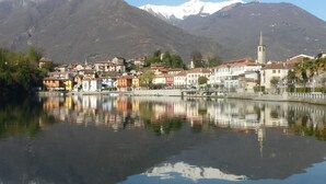 Un pueblo a orillas del lago con edificios reflejándose en el agua, una imponente torre de iglesia y montañas nevadas al fondo.