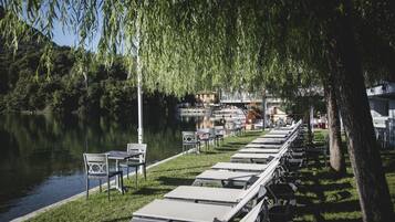 Un espace aménagé au bord du lac, avec des tables et des chaises, une pelouse verdoyante et une vue sur un bâtiment situé de l’autre côté de l’eau.