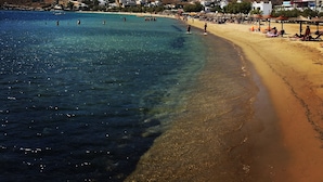 Una playa con agua cristalina, orilla arenosa y edificios al fondo.