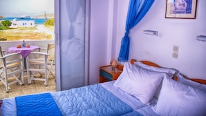 Habitación de hotel con una cama, una mesita con sillas, una mesita de noche y vista al mar.
