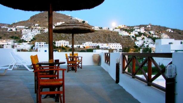 Una terraza con una mesa y sillas, un toldo de paja y vistas a edificios blancos en una colina.