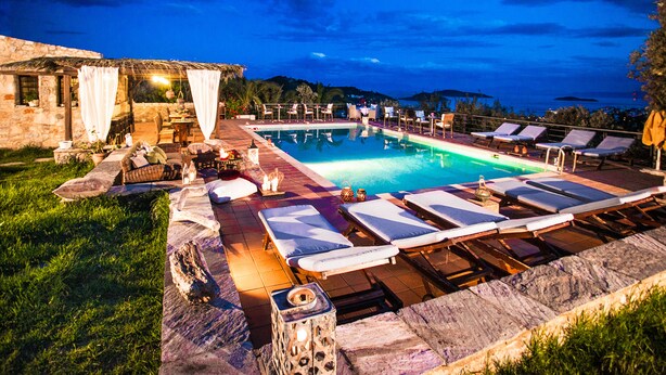 A poolside area with lounge chairs, a stone building, and a clear view of the water. - Vigles Sea View (Skiathos)