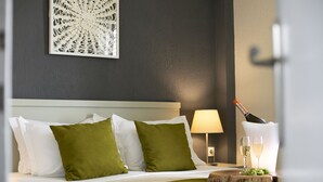 A neatly made bed with white and green pillows, a wooden headboard, a wall art piece, a bedside lamp, and a bottle of champagne with glasses on a wooden tray. - Vigles Sea View (Skiathos)