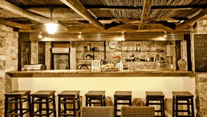 A rustic bar area with wooden stools, a stone wall, and a chalkboard menu. - Vigles Sea View (Skiathos)