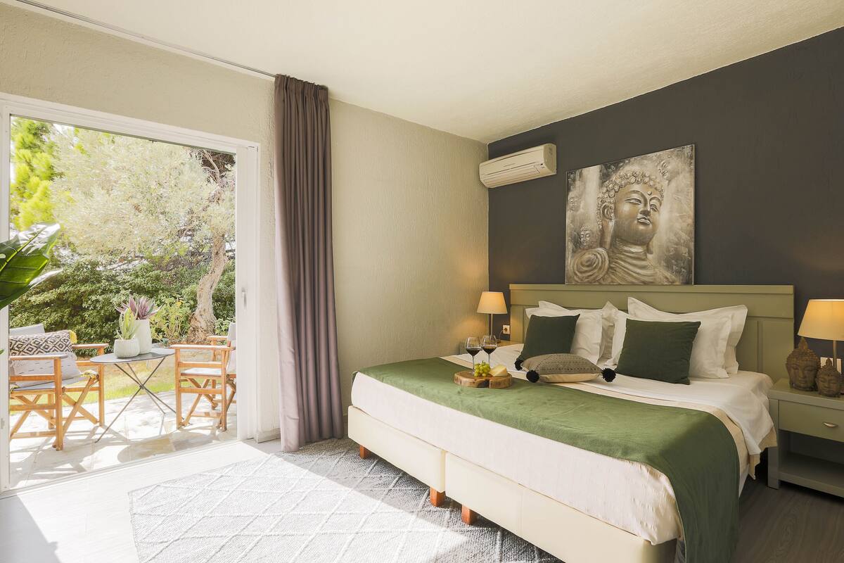 Une chambre à coucher avec un lit, des tables de chevet, une fenêtre et une vue sur la verdure.