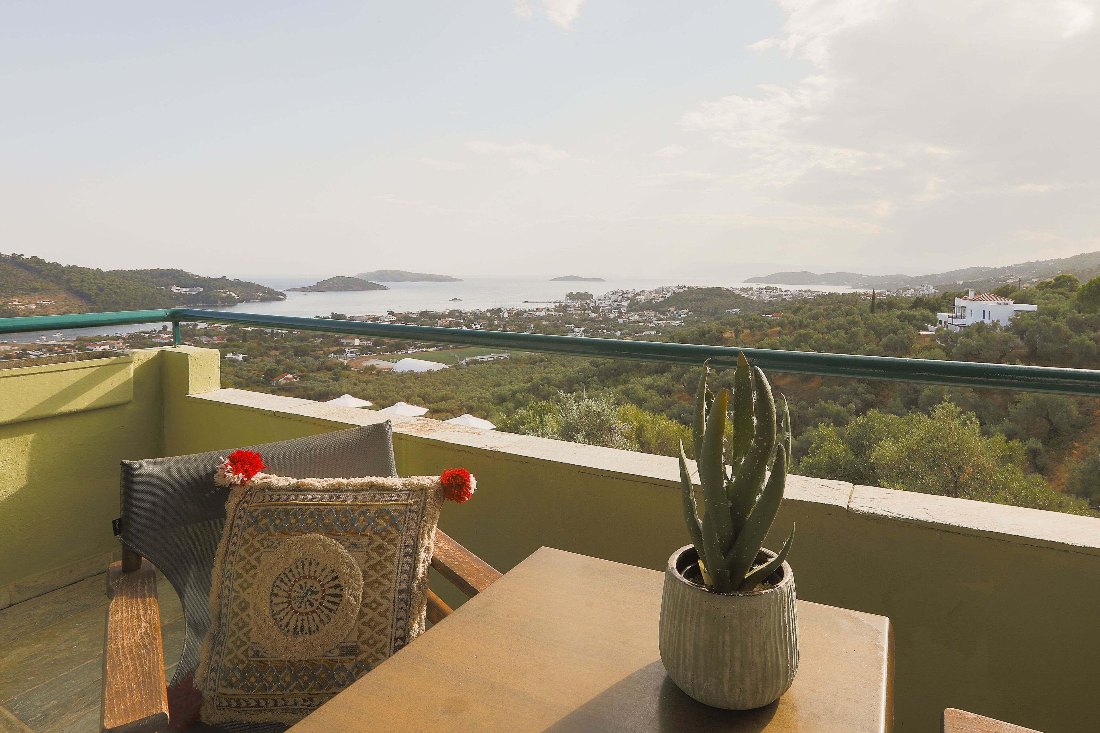 A balcony with a view of a coastal landscape, a cactus plant, and a patterned cushion.