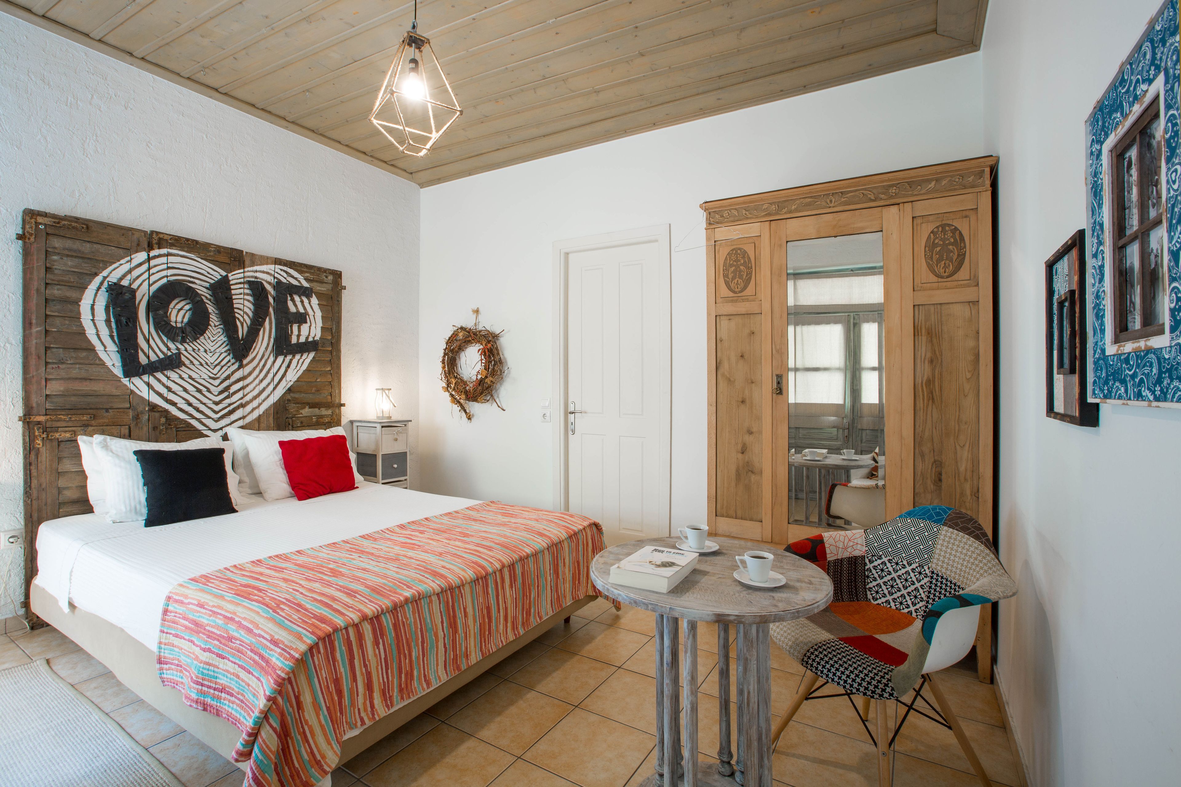 A bedroom with a bed, a small round table with a cup and saucer, a chair, a wardrobe, and a wall decoration with the word "LOVE".