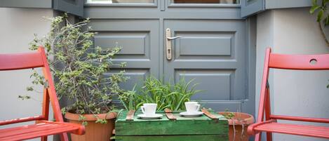 Un cofre de madera verde con dos tazas y platillos blancos encima, frente a una puerta gris con un picaporte.