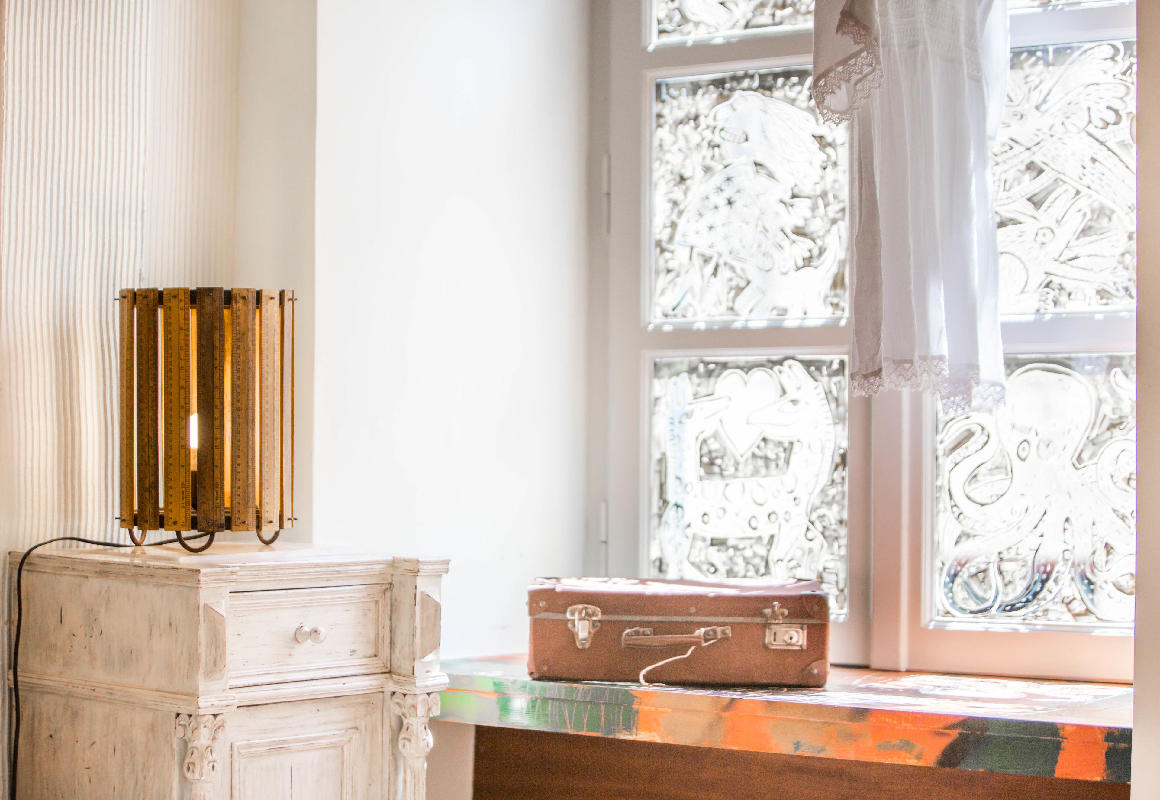 A vintage-style dresser with a brass thermometer, a brown suitcase on top, and a window with intricate patterns.