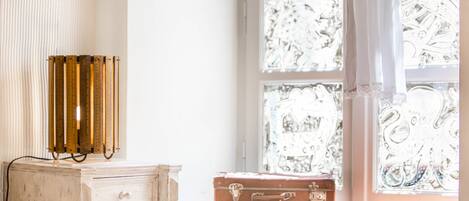 A vintage-style dresser with a brass thermometer, a brown suitcase on top, and a window with intricate patterns.