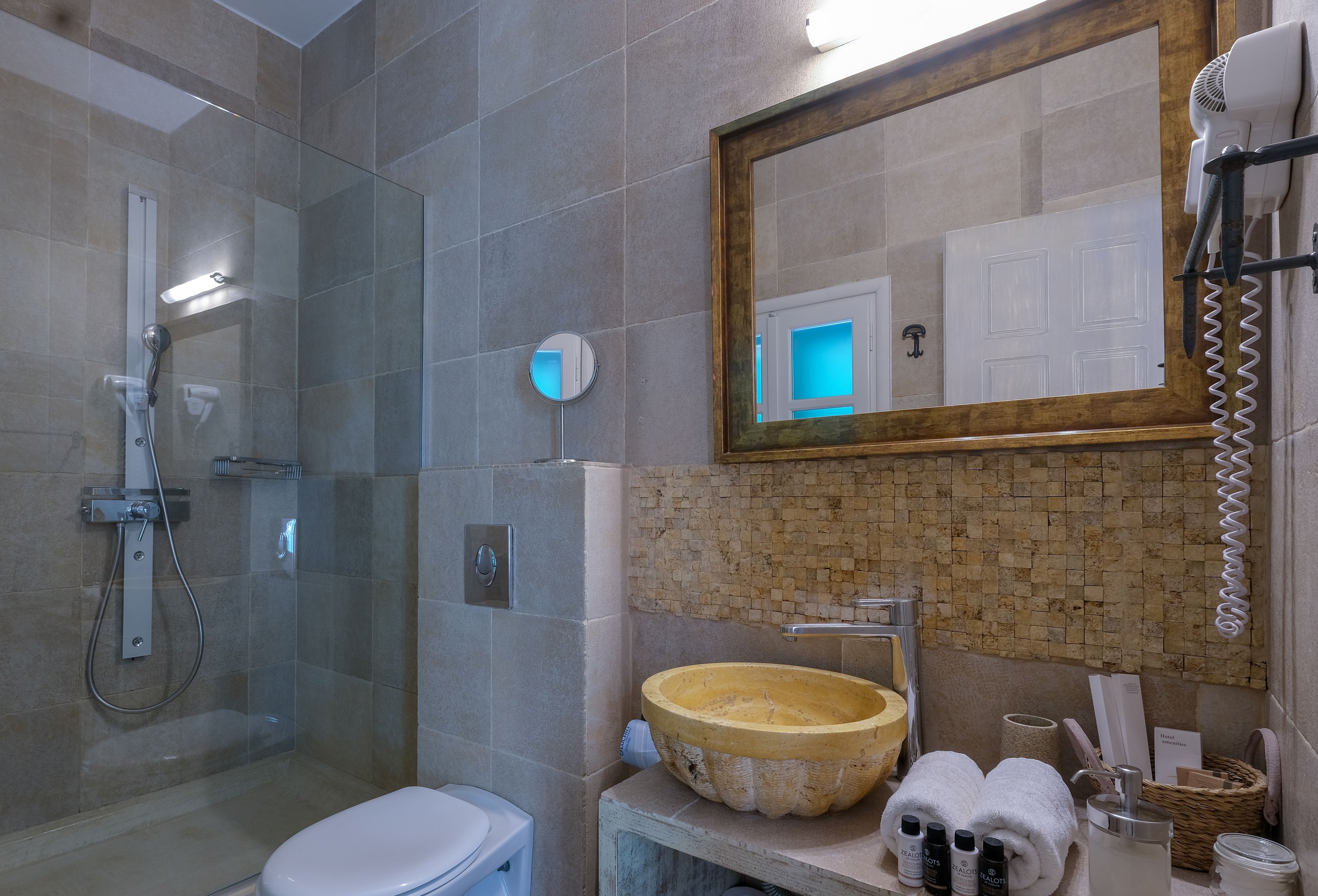 A bathroom with a glass-enclosed shower, a white toilet, a large round sink, and a mirror above the sink.