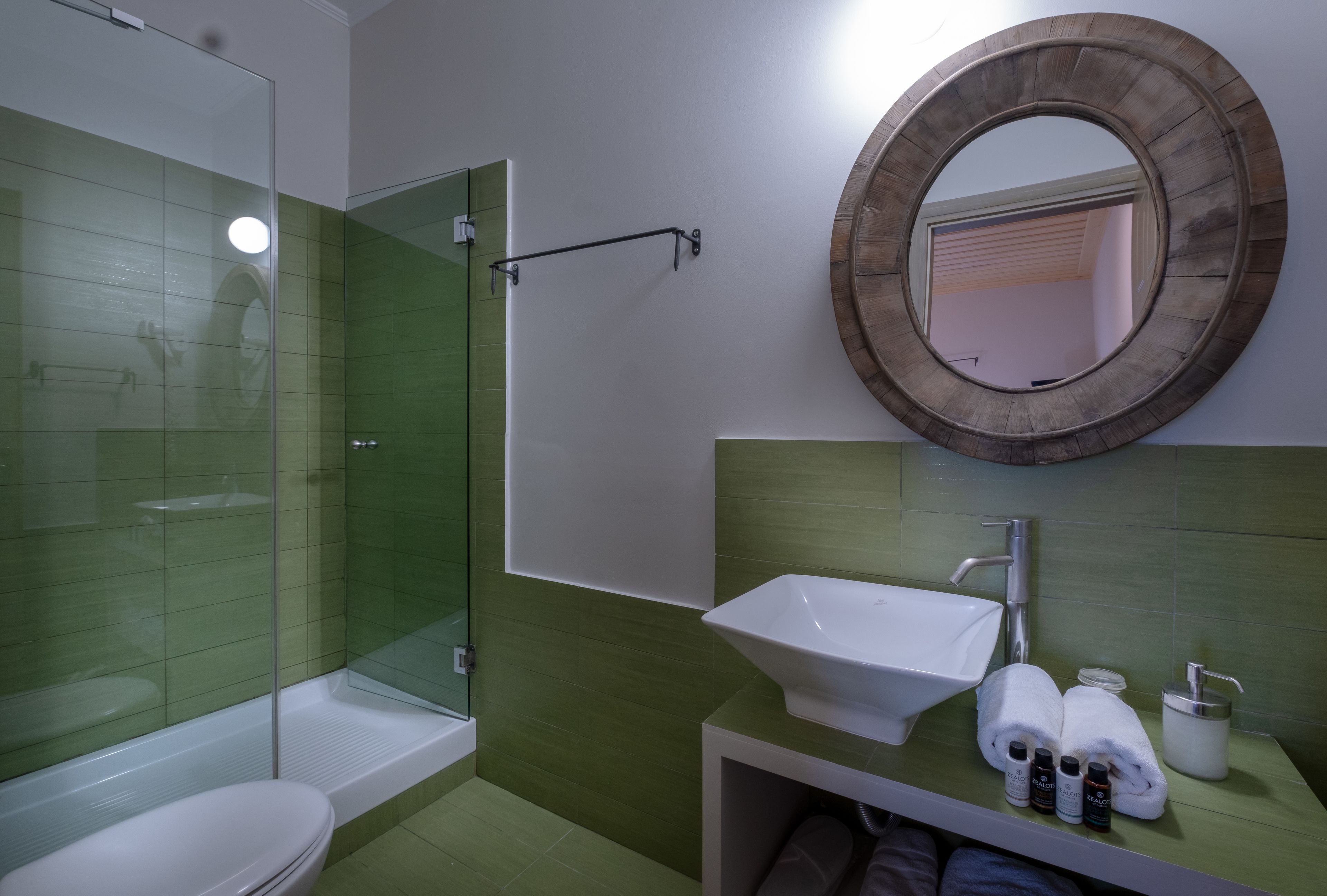 A bathroom with a glass shower enclosure, a white sink, and a round mirror.
