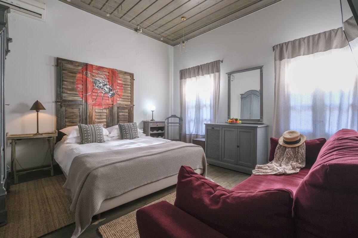 A bedroom with a bed, a dresser, a mirror, a red sofa, and a wall with a red and black artwork.