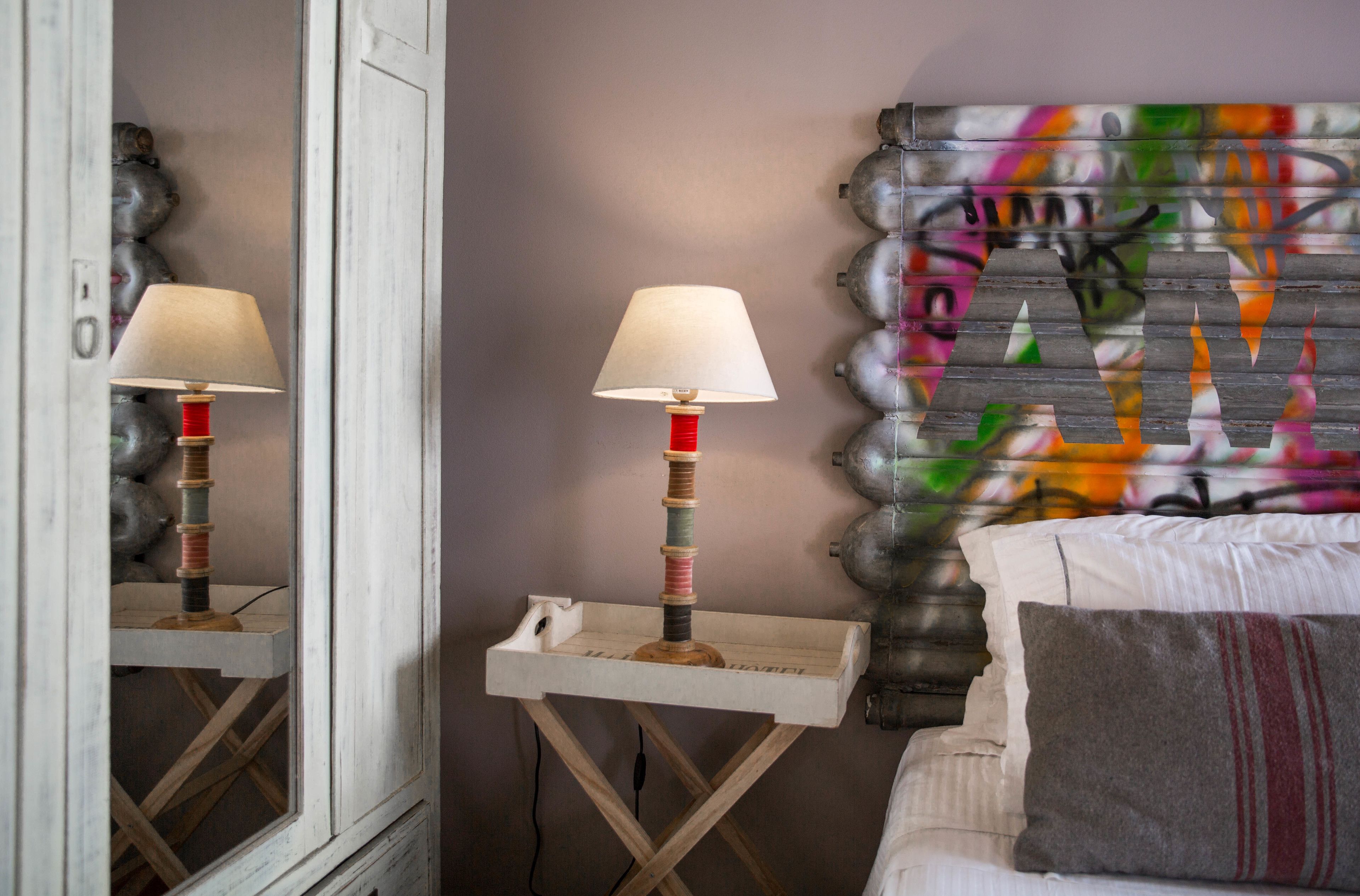A room with a bed, a small table with a lamp, and a mirror.