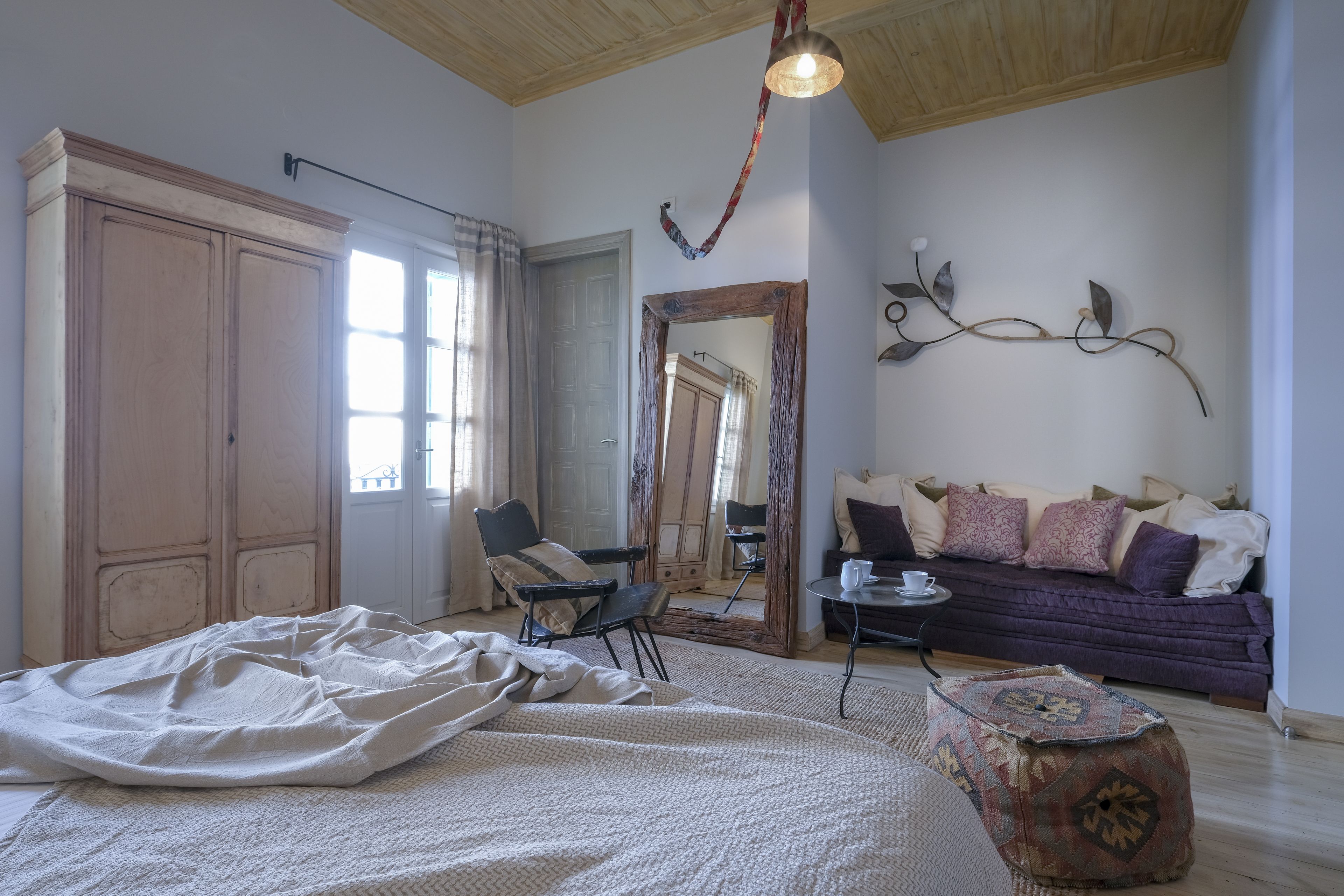 A room with a bed, a chair, a sofa, a mirror, and a table.
